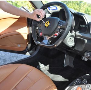 A technician cleaning the steering wheel and dashboard of a sports car with a tan leather interior.